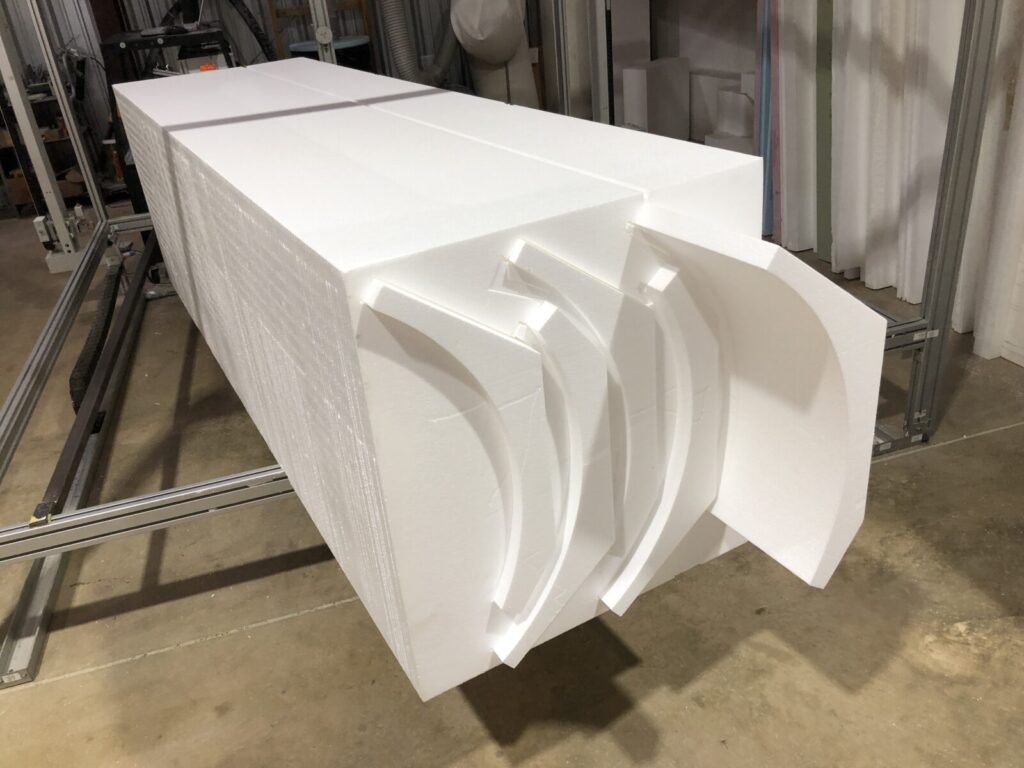 Large white foam blocks with several curved foam pieces partially separated, placed on a metal frame in an industrial setting.