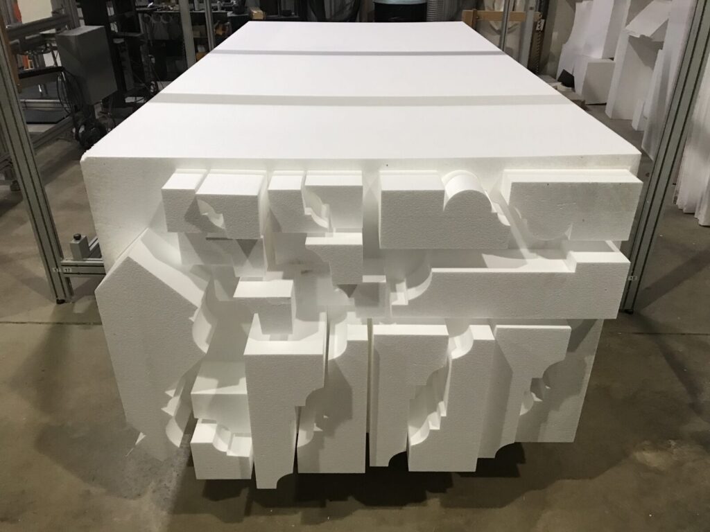 Large white blocks of Styrofoam stacked together, each with irregular geometric cutouts, in an industrial setting.