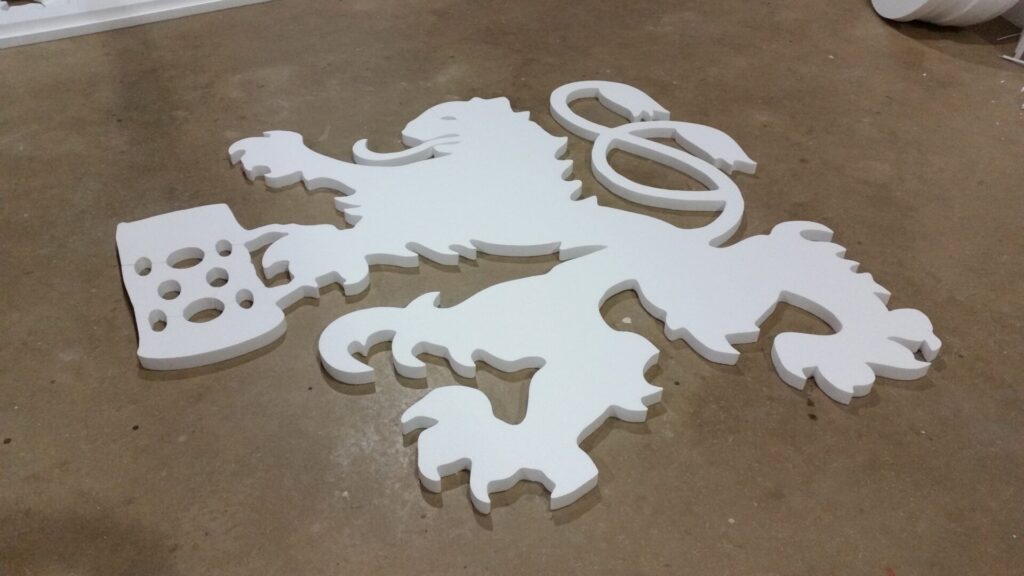 A white, flat, three-dimensional lion emblem with a paw holding a shield lies on a concrete floor.