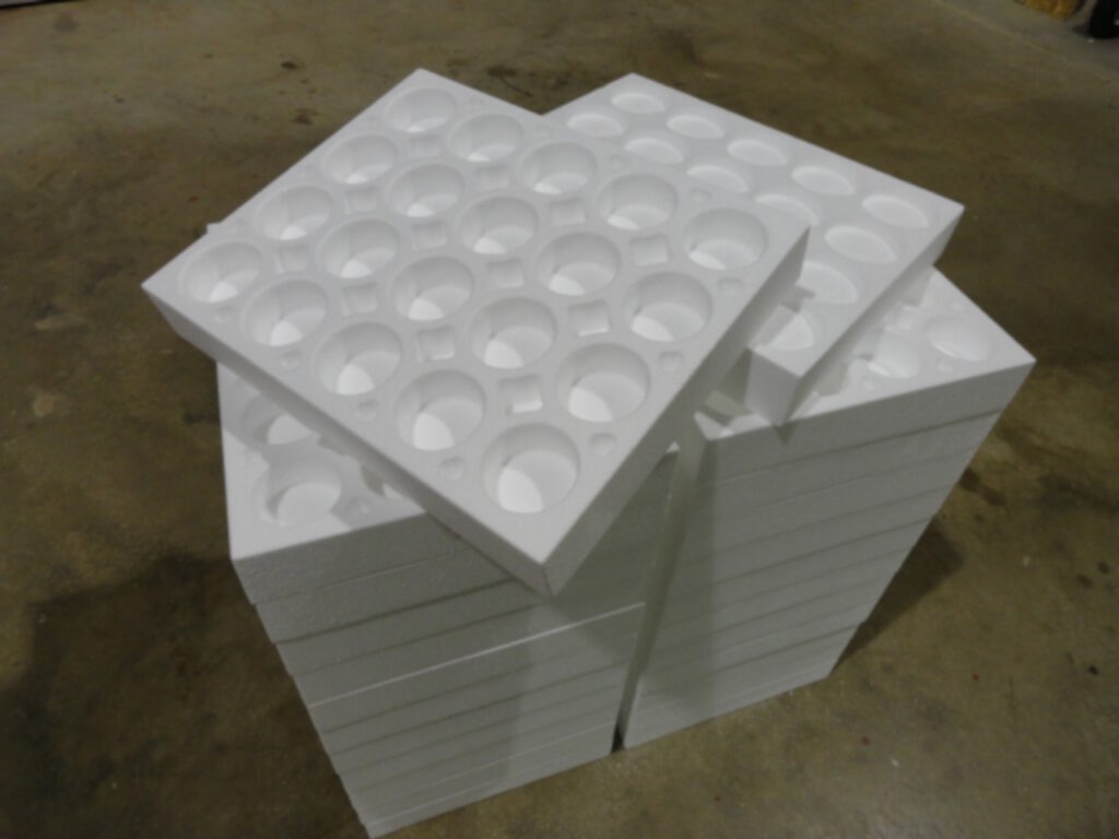 Stack of white foam trays with circular indentations, placed on a concrete floor.