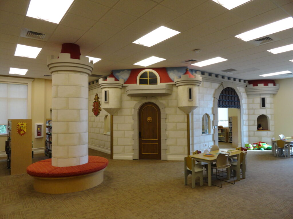 Children’s library area featuring a large castle-themed play structure, tables, chairs, and bookshelves.